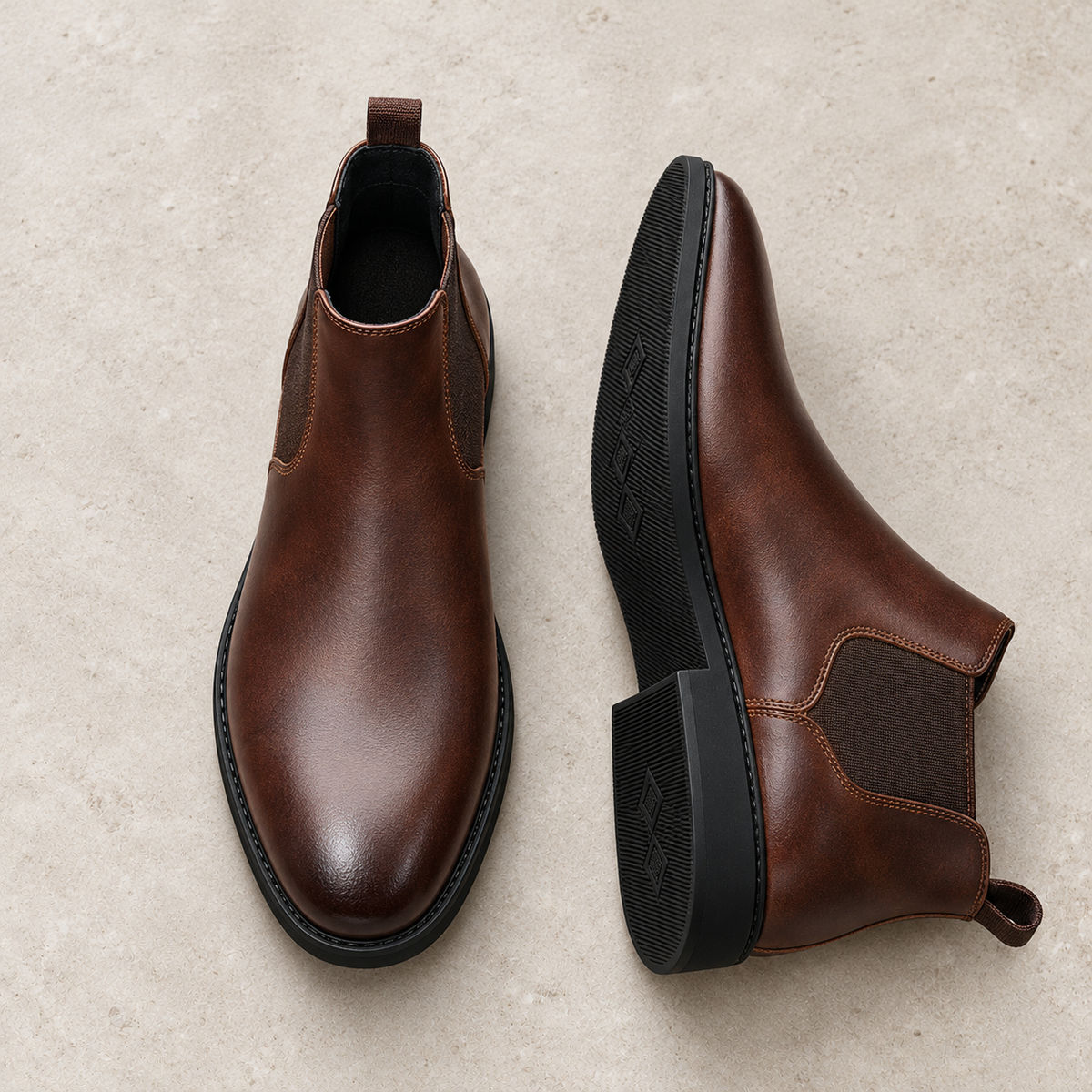 A pair of brown Chelsea ankle boots on pale limestone, showing the upper and sole.