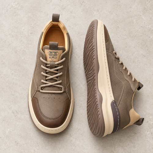 A pair of brown leather casual sneakers on pale limestone, showing the upper and sole.